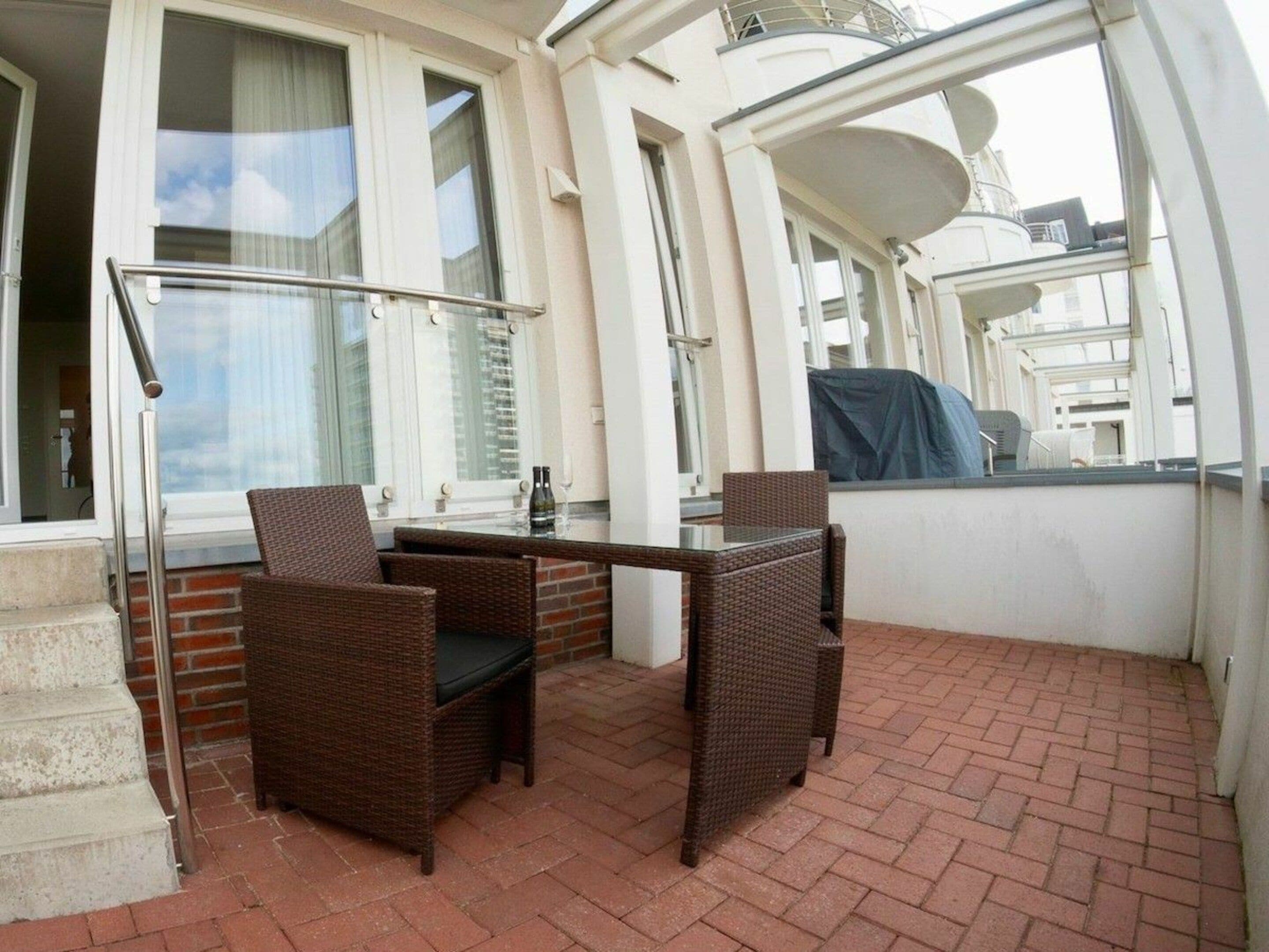 Een balkon met rieten meubels, een glazen tafel en uitzicht op zee.