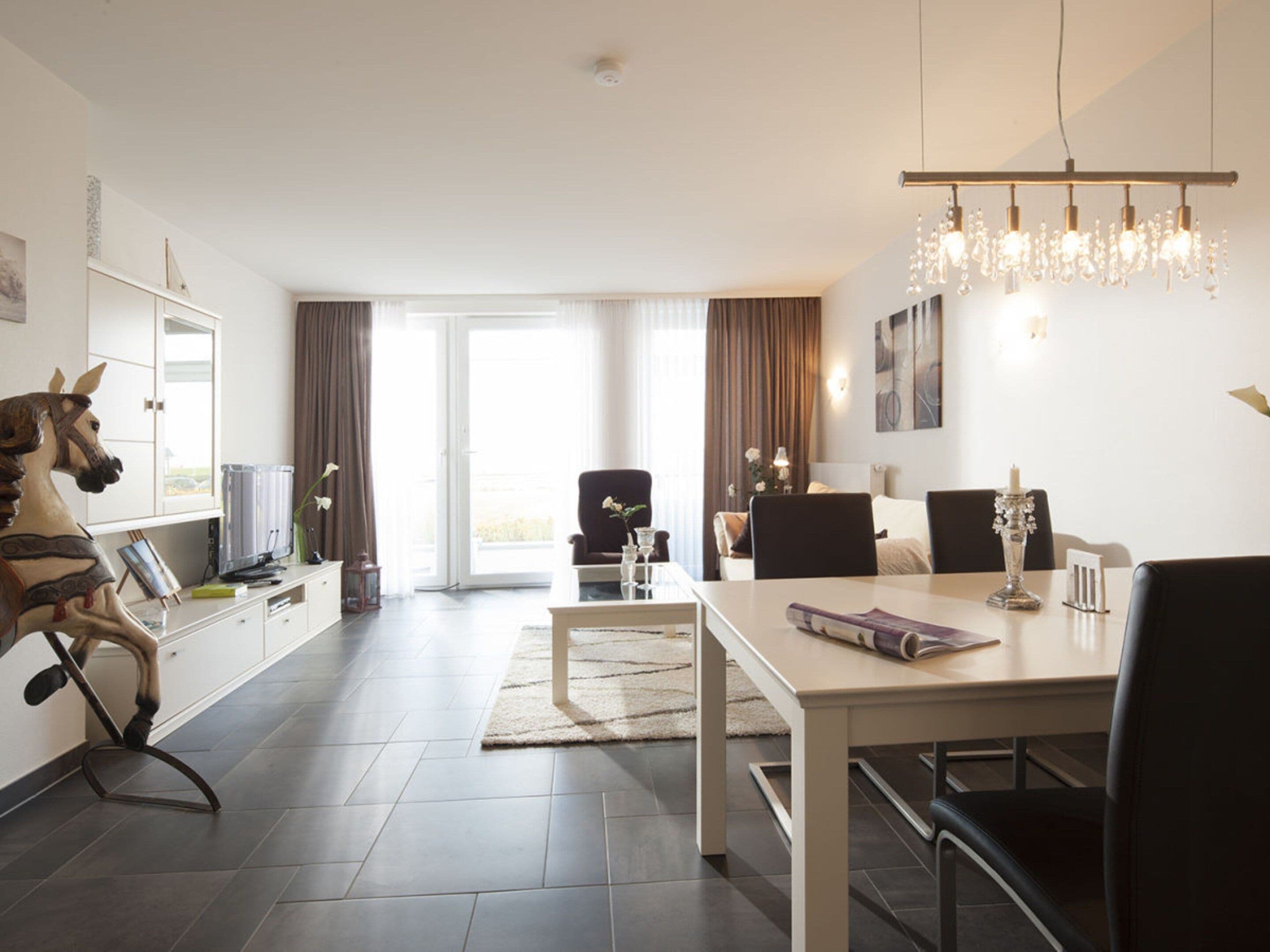 A modern hotel room with a dining area, a chandelier, and a large window with curtains.