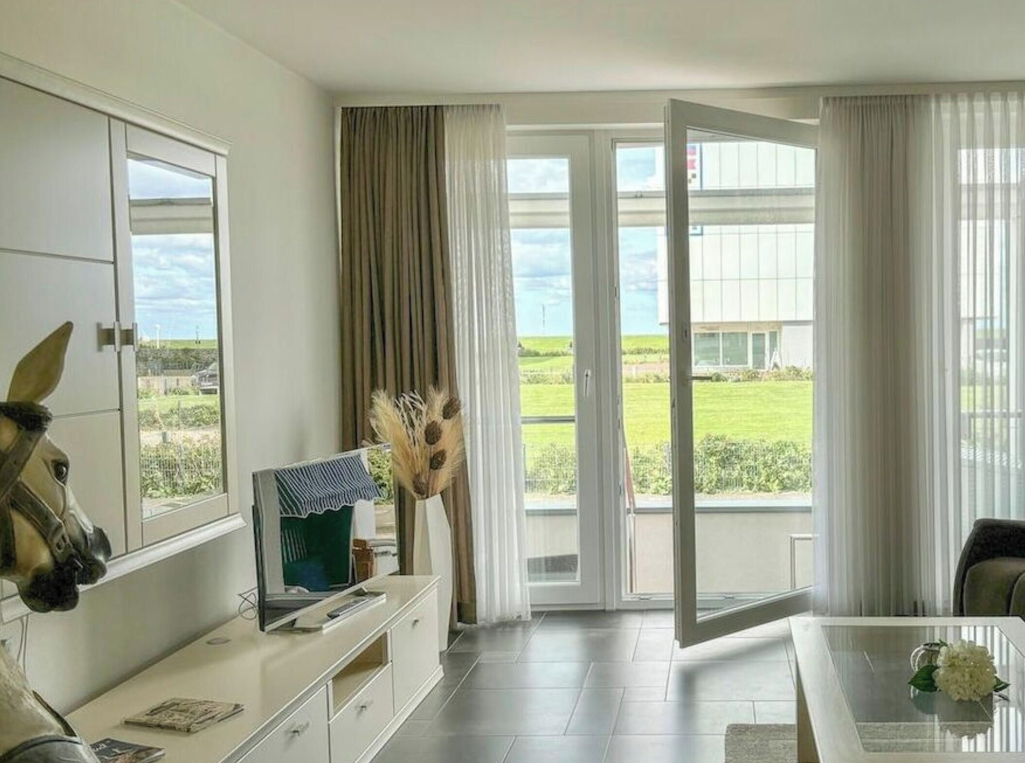 A hotel room with a large window, a desk, a chair, and a horse head decoration.
