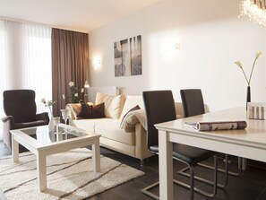 Ein modernes Wohnzimmer mit einer Couch, zwei Sesseln, einem Couchtisch und einem Esstisch.