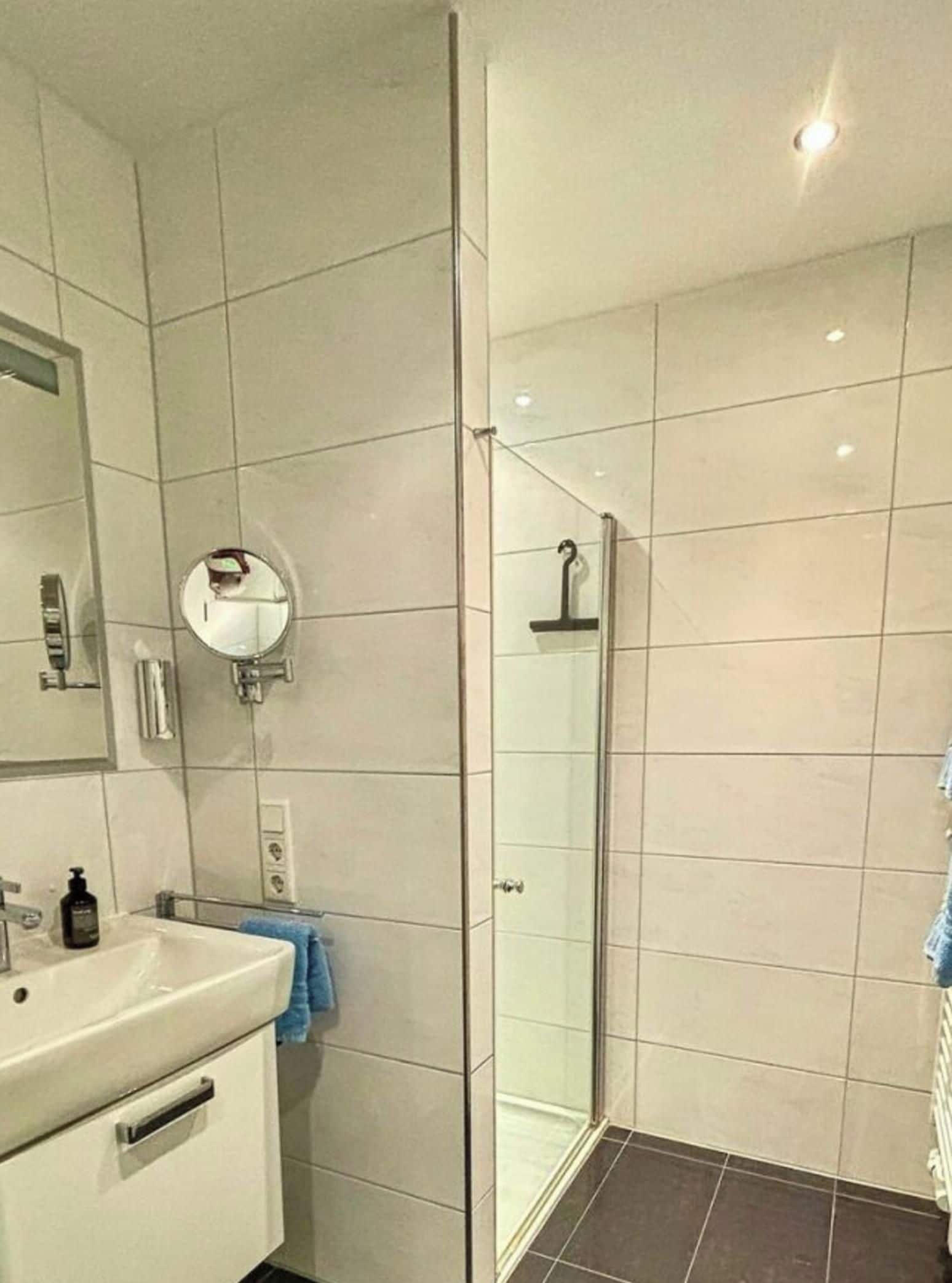 Ein modernes Badezimmer mit Duschkabine aus Glas, Waschbecken und Spiegel.
