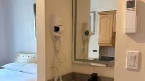 A bedroom with a bed, a bathroom with a sink, a mirror, and a hairdryer. - Lantern City Suites (Toronto)