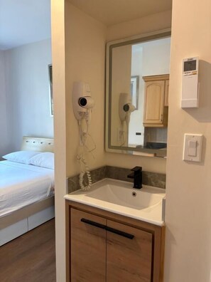 Een slaapkamer met een bed, een badkamer met een wastafel, een spiegel en een haardroger.