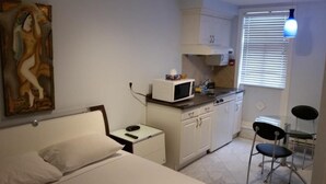 A compact room with a bed, a small bedside table, a microwave, a sink, and a chair. - Lantern City Suites (Toronto)