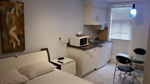 Een kleine kamer met een bed, een klein nachtkastje, een magnetron, een wastafel en een stoel.