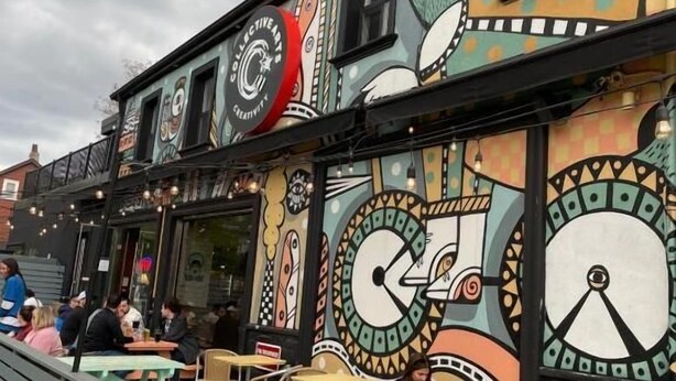 An outdoor seating area with tables and chairs, a building with artistic murals, and a clear sky. - Lantern City Suites (Toronto)