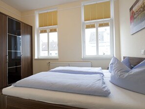 A bedroom with a bed, a wardrobe, and two windows with blinds. - Friedrichstr. 36 Apt. 7 (Norderney)