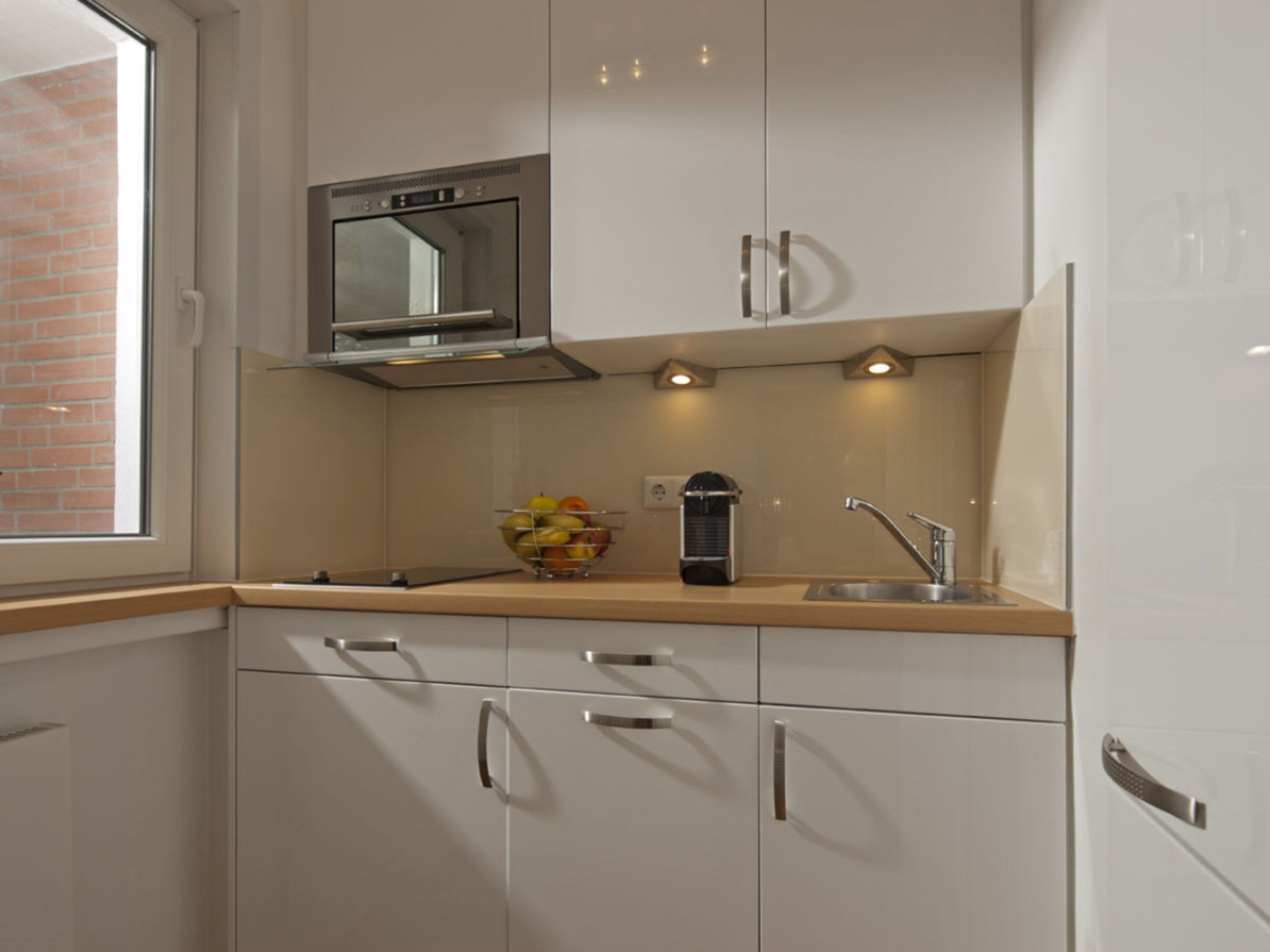A compact kitchen with a built-in microwave, a sink, and a fruit bowl on the countertop.
