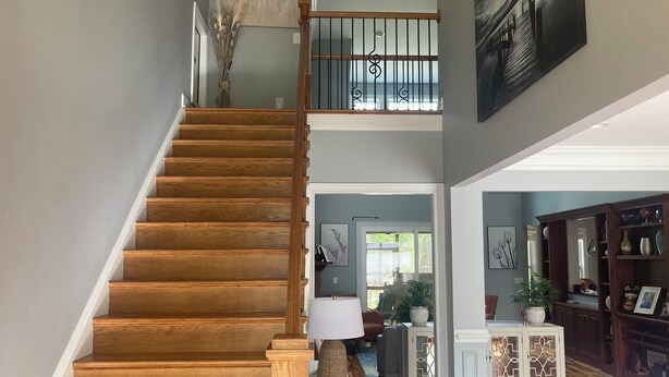A wooden staircase leading to a second floor with a railing, a dining area with a table and chairs, and a cabinet with decorative items.