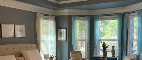 A bedroom with a large bed, a ceiling fan, and a view of the outdoors through windows.