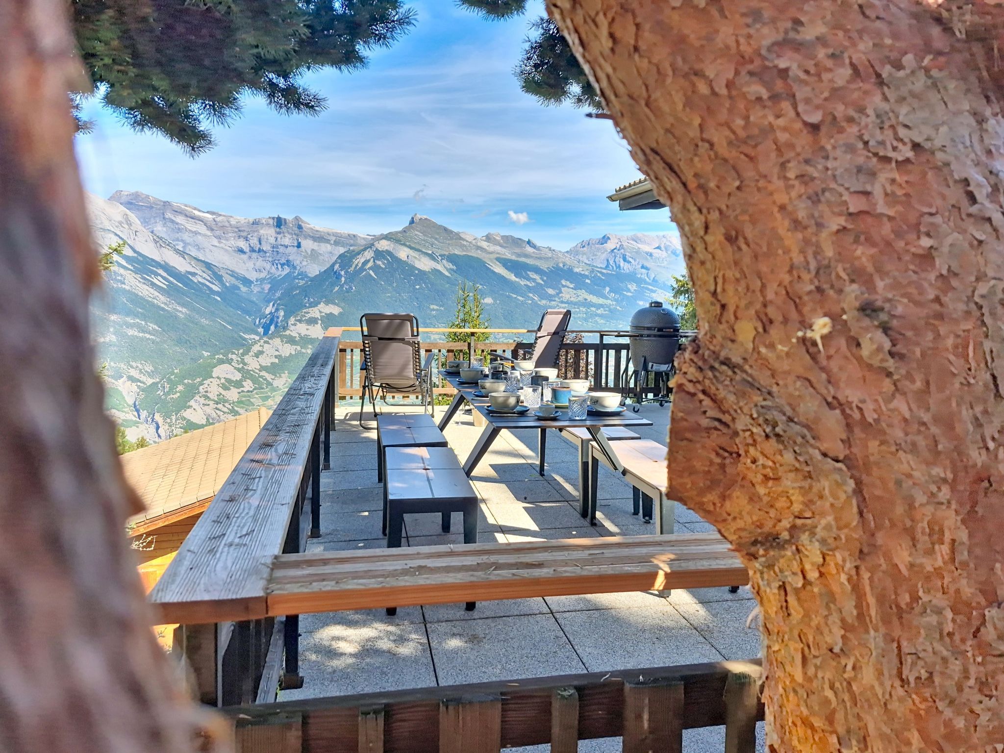 An outdoor dining area with a mountain view, wooden benches, and a barbecue grill.