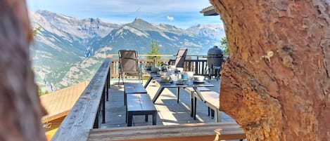 An outdoor dining area with a mountain view, wooden benches, and a barbecue grill.