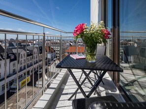 A balcony with a table, a vase with flowers, and a view of buildings. - Holiday Apartment in Norderney With Sauna (Norderney)