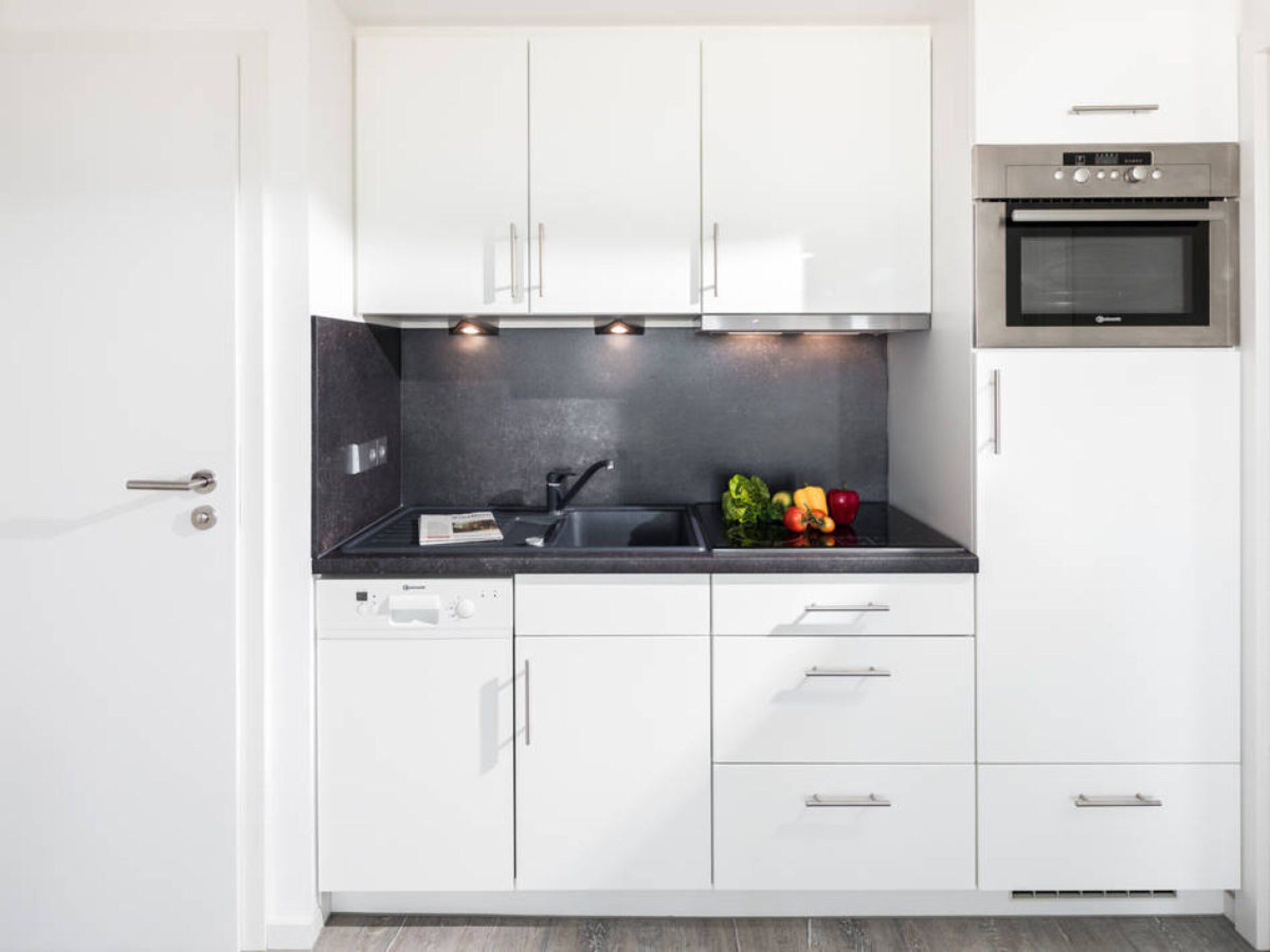 Une cuisine moderne avec des meubles blancs, un plan de travail noir, un four en acier inoxydable et un évier.