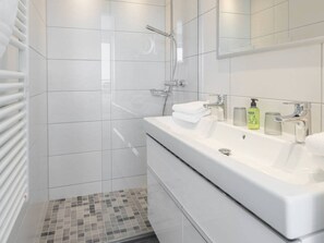 A modern bathroom with a walk-in shower, a large white sink, and a mirror above it. - Holiday Apartment in Norderney With Sauna (Norderney)