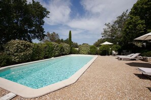 A rectangular swimming pool with a pebble-lined deck, surrounded by lush greenery and trees. - Peaceful Villa Haven in the Luberon (Beaumettes)