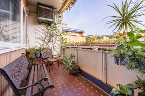 Ein Balkon mit einer hölzernen Bank, Blumentöpfen und Blick auf die umliegenden Gebäude.