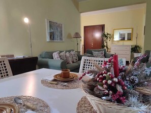 Ein Essbereich mit Tisch für zwei Personen, eine Couch im Hintergrund und eine Tür zu einem weiteren Raum.