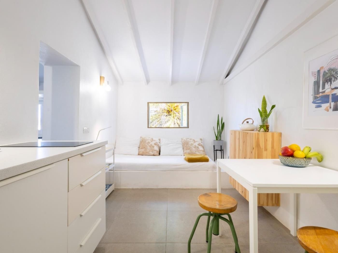Eine moderne Küche mit weißen Schränken, einem Holzhocker, einem kleinen Tisch und einer Obstschale.