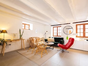 A spacious living area with a sofa, chairs, a coffee table, and a red chair. There are windows with wooden frames, a lamp, and a mirror on the wall. - Finca Santa Catalina · 3 casitas · Private plunge pool (La Guancha)