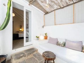 Ein Zimmer mit einem weißen Sofa, einem kleinen runden Holzschemel, einem Kaktus und einer Topfpflanze.