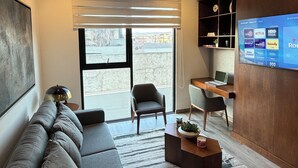 Un salon moderne avec un canapé, des fauteuils, une table basse et un téléviseur fixé au mur.