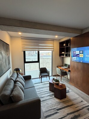 Een moderne woonkamer met een bank, stoelen, een salontafel en een aan de muur bevestigde televisie.