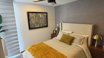 Een slaapkamer met een bed, een plafondventilator, een nachtkastje, een lamp en een schilderij aan de muur.