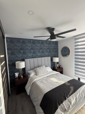 Een moderne slaapkamer met een bed, twee nachtkastjes, een plafondventilator en een raam met zonwering.