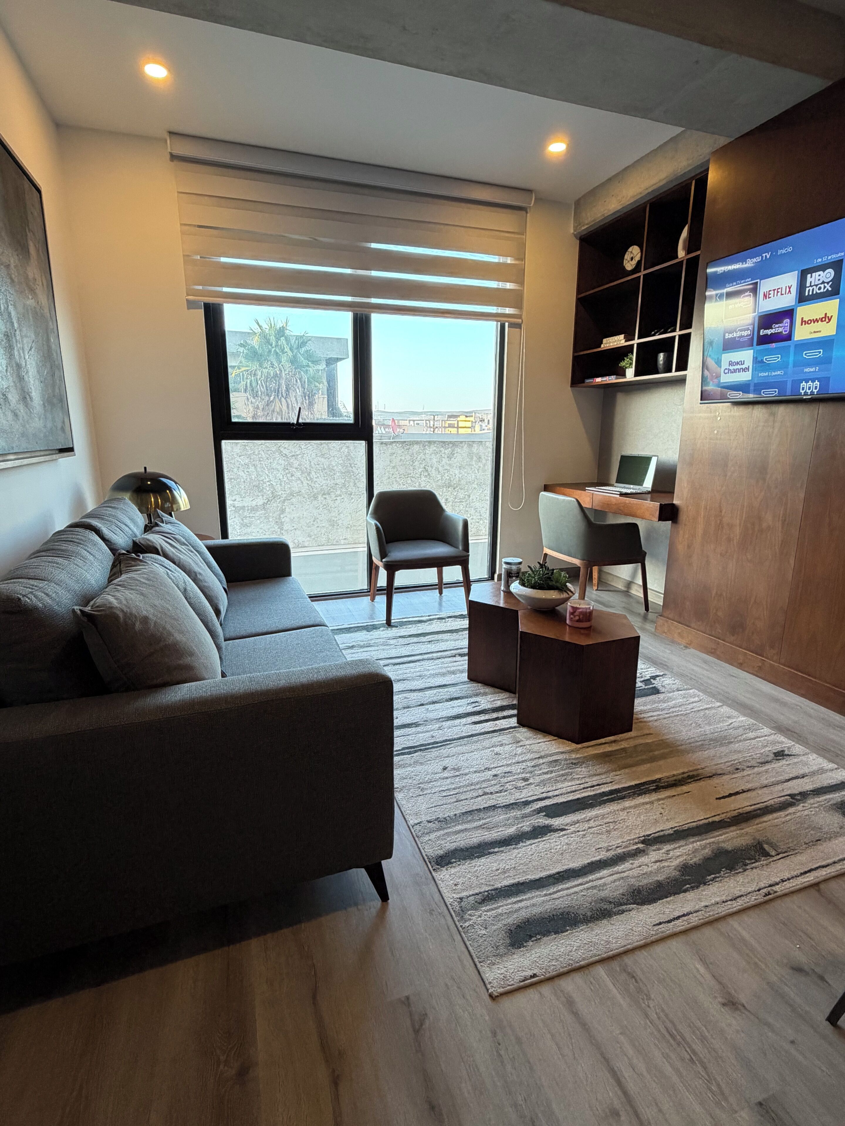 Ein modernes Wohnzimmer mit einer Couch, Sesseln, einem Couchtisch und einem Fernseher, der Streaming-Dienste anzeigt.
