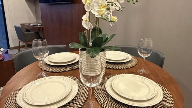 Une table de salle à manger ronde, ornée d’un vase rempli d’orchidées blanches, de plusieurs assiettes et de verres à vin.