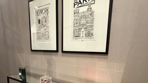 Un couloir avec une console, deux tableaux encadrés représentant des paysages urbains et une bougie décorative.