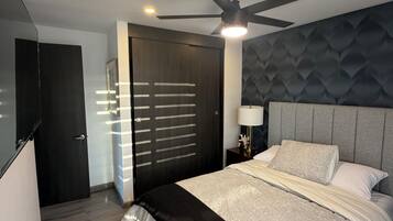 A modern bedroom with a bed, a ceiling fan, a nightstand, and a door.