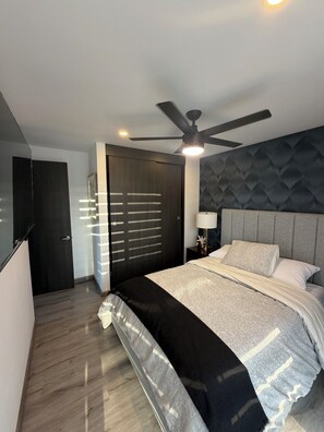 Ein modernes Schlafzimmer mit einem Bett, einem Deckenventilator, einem Nachttisch und einer Tür.