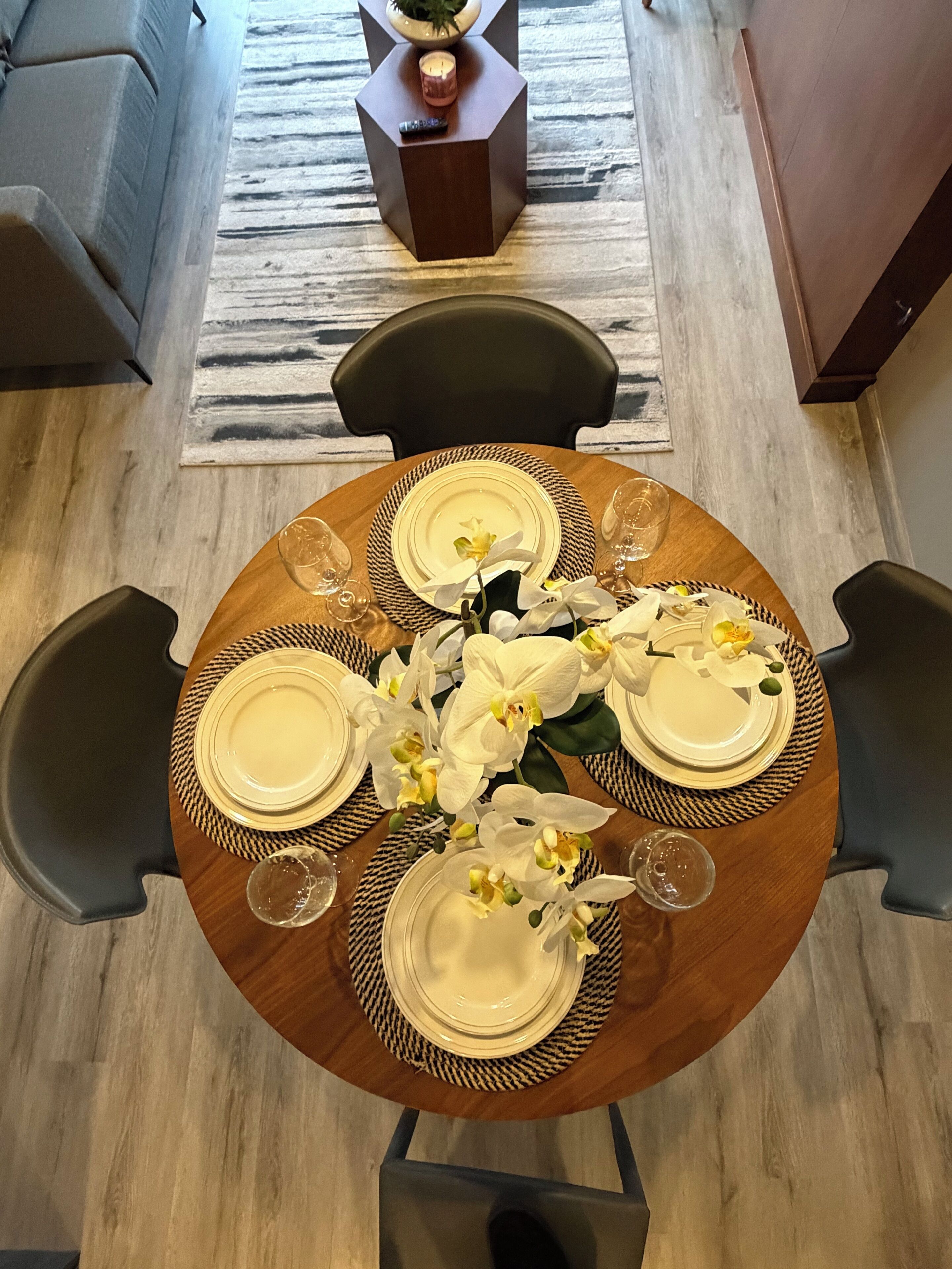 A round dining table with four chairs, white orchid flowers, and a candle on a side table.