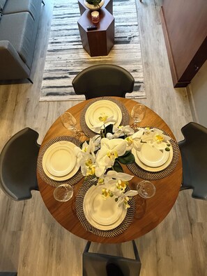 Ein runder Esstisch mit vier Stühlen, weißen Orchideen und einer Kerze auf einem Beistelltisch.