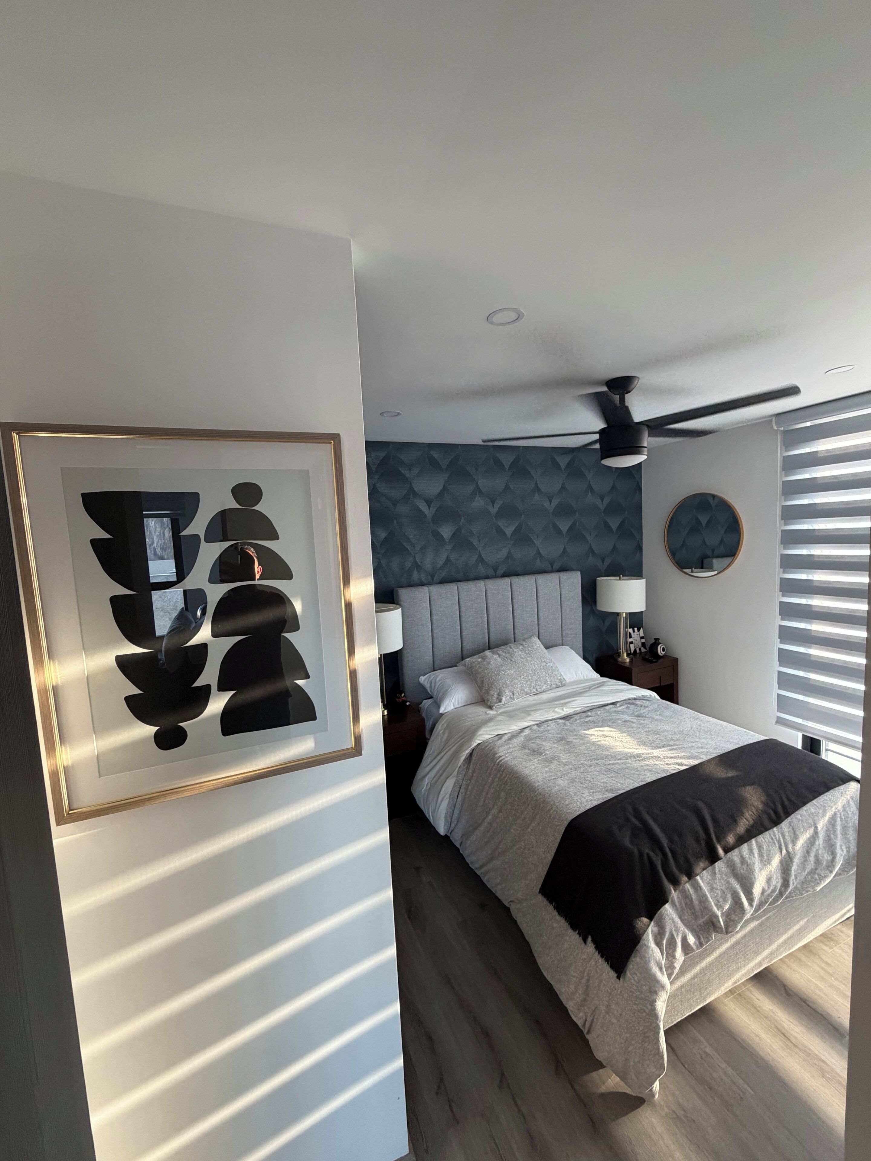 A bedroom with a bed, a ceiling fan, a nightstand, and a wall-mounted mirror.