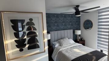 A bedroom with a bed, a ceiling fan, a nightstand, and a wall-mounted mirror.