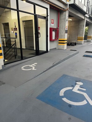 Een gevel met een glazen deur, een bord voor rolstoeltoegankelijkheid en een brandblusser.