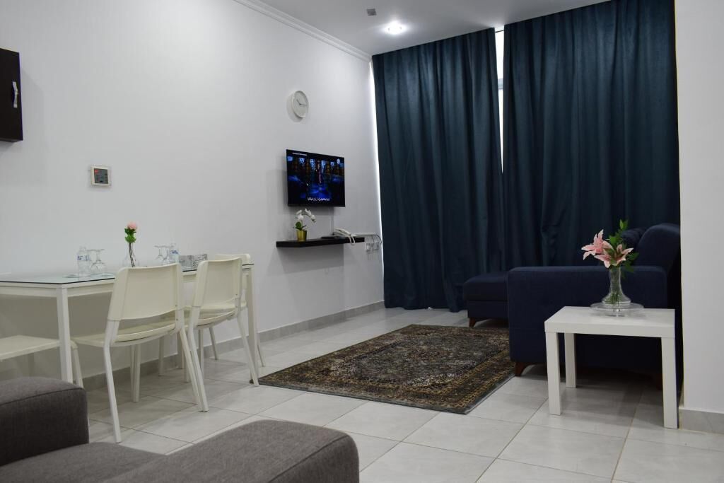 Ett modernt vardagsrum med en tv, en matplats med stolar, en soffa och ett litet bord med en vas.