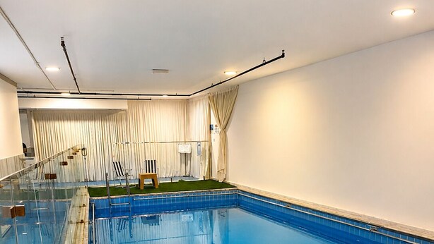 A swimming pool with clear water, surrounded by a glass barrier and metal railings. - Atlantis Hotel Suite & Apartment (Salmiya)