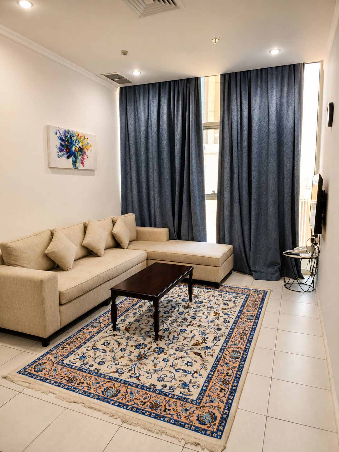 A living room with a beige sectional sofa, a dark coffee table, and a patterned rug.