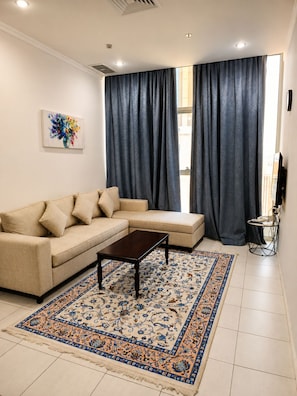 A living room with a beige sectional sofa, a dark coffee table, and a patterned rug. - Atlantis Hotel Suite & Apartment (Salmiya)