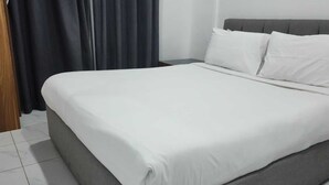 A bed with a grey headboard and white bedding in a room with a wooden door and dark curtains. - Atlantis Hotel Suite & Apartment (Salmiya)