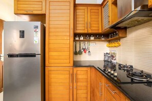 Eine Küche mit Holzausstattung, einem Edelstahlkühlschrank, hängenden Kochutensilien und einem Gasherd.