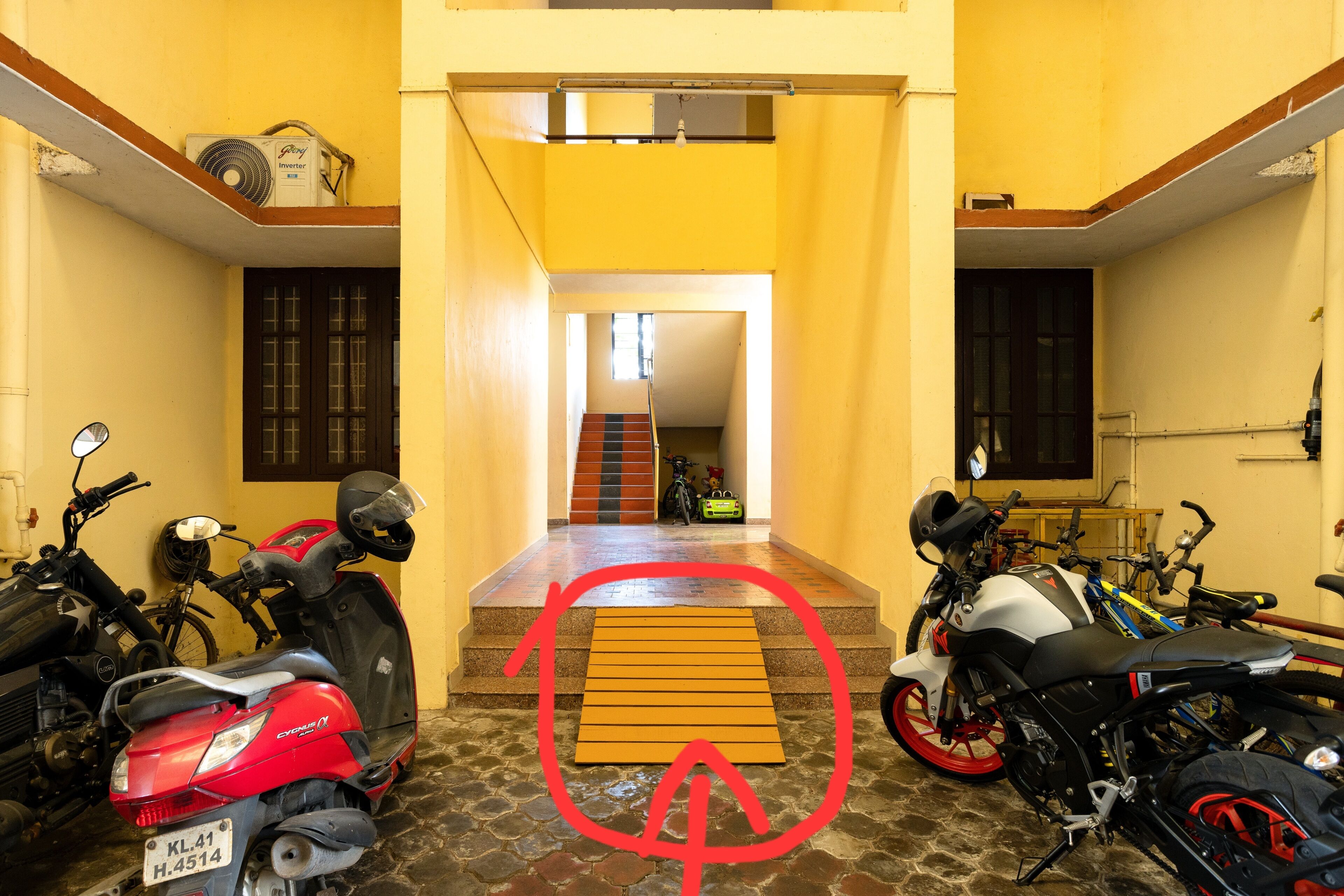 A motorcycle garage with multiple bikes, a staircase leading to an upper level, and a yellow wall.
