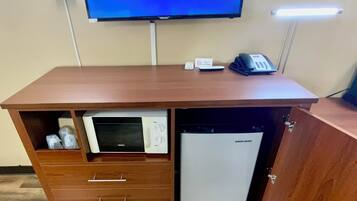 A hotel room with a television displaying a schedule, a desk with a telephone, and a built-in mini-fridge.