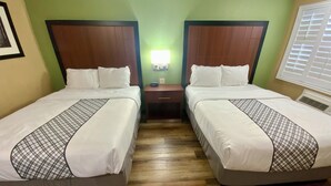 A hotel room with two beds, a nightstand, a wall-mounted lamp, and a window with blinds. - Cozy 2 Queen Suite 128–Stroll Historic Downtown Great Restaurants & Unique Shops (Grants Pass)