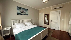 Quarto de hotel com cama, mesas de cabeceira, um quadro, uma porta e um aparelho de ar condicionado.