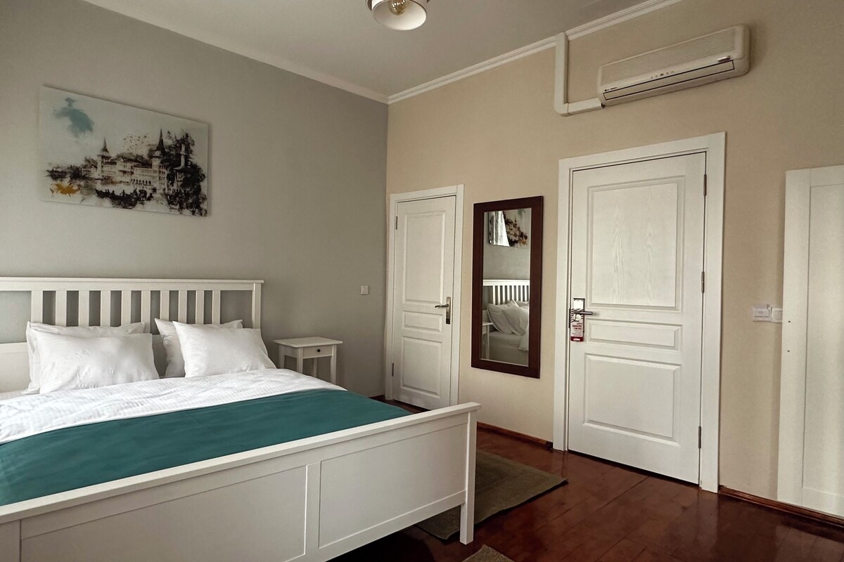 A bedroom with a bed, bedside tables, a mirror, and a door.